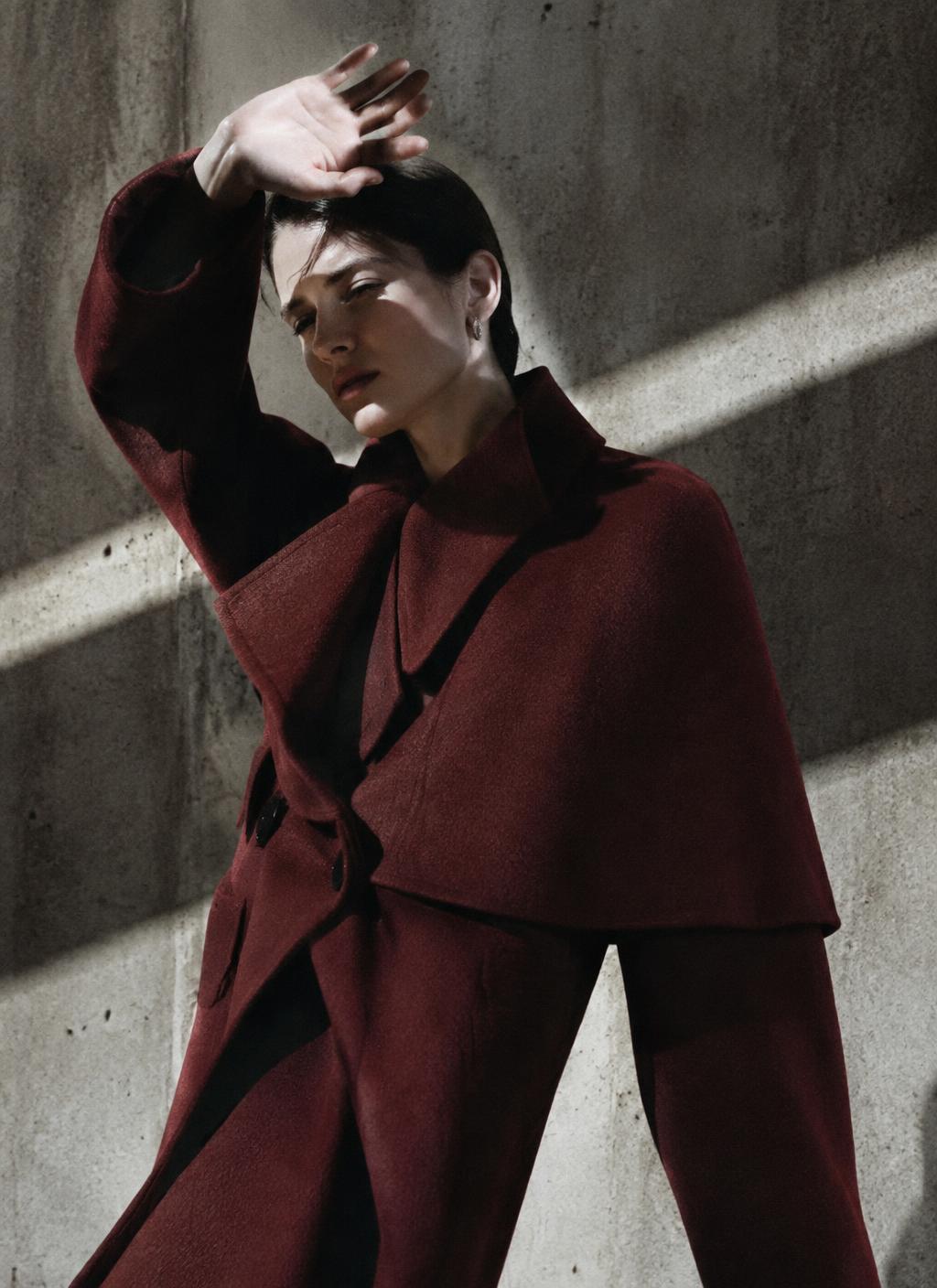 Model in an oxblood cape coat against concrete